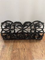 Front view of black ornate cast iron planter box with leafy vine design and lattice base