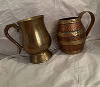 Side view showing the solid brass mug with smooth finish next to the hammered copper and brass banded mug.