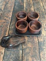 Photo showing the set of 4 round wooden bowls on a black tray with the carved wooden duck placed beside it on a rustic wooden surface.