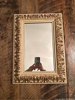 Front view of rectangular mirror with ornate carved wood frame in gold and beige distressed finish.