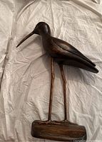 Side view of bird carving showing elongated neck and beak on wooden base.