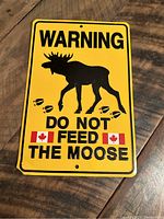 Front of yellow metal warning sign with black moose silhouette, text, and Canadian flags.