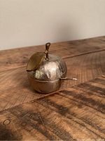 Honey pot shaped like an apple with a lid and bronze leaf and stem, sitting closed on a wooden surface.