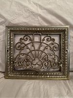 Front view of the ornate antique cast iron wall register with an intricate scrollwork design in silver finish.