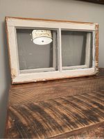 Vintage wooden window with white paint, showing wear and two glass panes, sitting on wooden surface