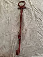 Full length of red metal reacher/grabber with circular handle and claw grip on white background.