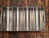 Top-down view of stainless steel cutlery holder showing four compartments and handles.
