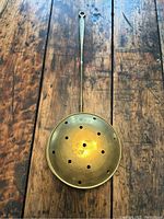Top view of the solid brass bed warmer showing the perforated round pan and long handle on a wooden surface.