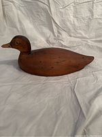 Left side angled view of vintage wooden duck decoy showing the profile with smooth brown wood and visible wear marks.