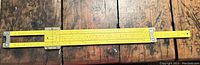All metal yellow Pickett slide rule with sliding center section on wood surface