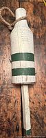 Front view of the wooden buoy showing white paint and two green horizontal stripes with rope attached