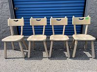 Four wooden chairs with light natural finish arranged in a row outdoors.