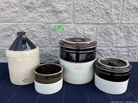 Four stoneware crocks displayed on a table, showing size variations and lids on two of them