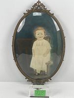 Full view of the ornate oval metal frame with convex glass and hand-tinted photograph of a child