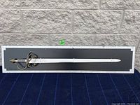 Full view of decorative knight sword mounted on rectangular black wooden display board.