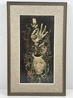 Framed surreal print showing a hand holding a rose and a face surrounded by abstract design, vintage frame with cloth lining visible.