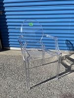 Front-side view of clear acrylic ghost chair with round backrest and armrests, showing overall shape and transparency.