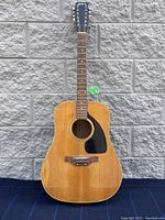 Front full body view of 12-string acoustic guitar with natural wood finish and black pickguard.