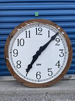 Full front view of large round IBM clock showing molded glass face, black numerals, wooden frame