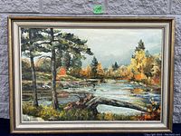 Photo of large autumn landscape painting with river, trees, and fall foliage, in gold-colored frame.
