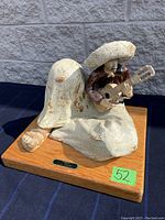 Wide shot showing full seated ceramic sculpture of Mexican troubadour on wooden base.