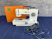 Front view of PFAFF 1209 compact sewing machine with foot pedal and orange carrying case