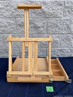 Front and side view of the wooden portable artist easel showing adjustable upright support and built-in storage compartment open on the side.