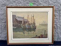 Overall front view of framed seascape painting showing multiple boats moored at industrial dock under soft lighting.