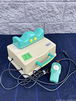 View of the entire Sun Ancon Chi Machine showing beige base with teal foot holder and wired remote control with dial.