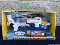 Front angle view of the Tonka Mighty Motorized Rescue Helicopter in original yellow and blue box with rescue basket accessory visible in packaging.