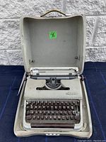 Front view of Olympia Deluxe typewriter inside original hard shell carrying case, showing keyboard and mechanical lever components.