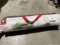 Photo of wrapped 3-person dome tent in gray bag with red carry strap, showing tent illustration and product info printed on bag.
