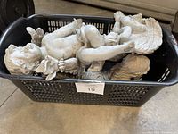 Four angel garden statues posed differently with visible wear and peeling paint in a plastic crate