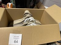Box containing multiple beige and white plastic clothes hangers stacked horizontally.