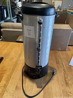 Front view of large stainless steel coffee urn with power cord and dispensing spout