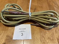Full view of coiled Fender Custom Shop guitar cord with braided cloth covering on wooden surface.