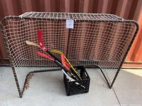 Photo of hockey net with white netting and brown metal frame. Several hockey sticks in black crate in front of net, showing varying colors and wear.