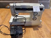 Front view of Kenmore sewing machine showing brand, stitch pattern panel, two dials and reverse lever, along with power cord and foot pedal in front.