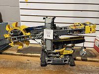 Front and side view of assembled yellow and dark bluish-gray LEGO Technic excavator showing rotating bucket wheel and tracked base
