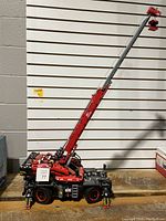 Side view of assembled red and black LEGO Technic mobile crane with extended boom on wooden surface
