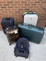 Front and side view of five pieces of luggage and backpack placed on concrete floor against a brick wall.