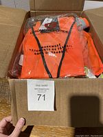 Box containing several reflective safety vests and harnesses including a packaged Ground Force orange mesh vest.