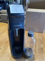 Front view of black SodaStream soda maker with clear plastic carbonating bottle showing branding and front details including carbonation nozzle.