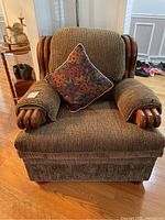 Front view of large upholstered armchair with wooden trim and floral pillow.