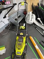 Front view of the Ryobi cordless mower showing deck, wheels, and handlebar upright