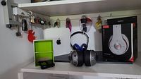 Shelf with Apple modem, headphones (one boxed white, one silver black), box with chargers, keys hanging on hooks