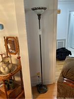 Full view of metal floor lamp standing next to a wooden chair and shelf.