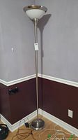 Full view of the tall brushed chrome floor lamp with white glass shade against a wall corner.
