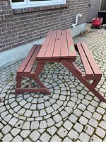 Foldable picnic table and benches shown set up on stone pavement, viewed diagonally with umbrella hole visible on tabletop.