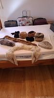 View of all fur accessories arranged on a bed with three suitcases in background, showing hats, headbands, ear muffs, stole, and collar.